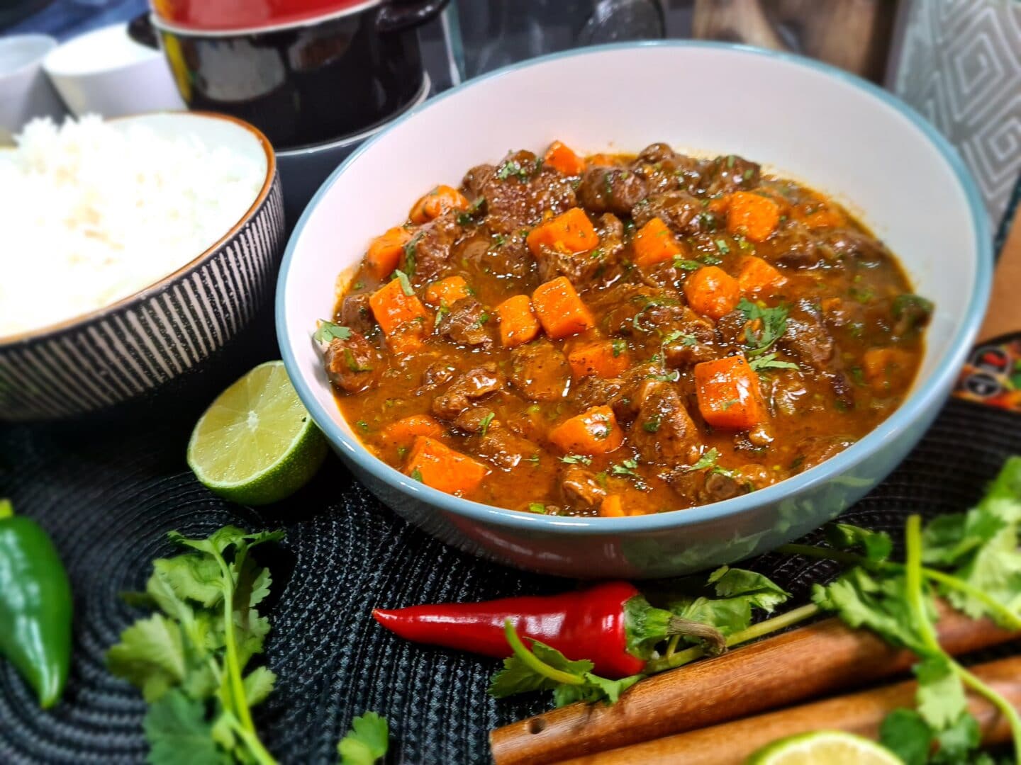 Bowl of Moroccan Coconut, Beef and Sweet Potato Curry surrounded by garnish
