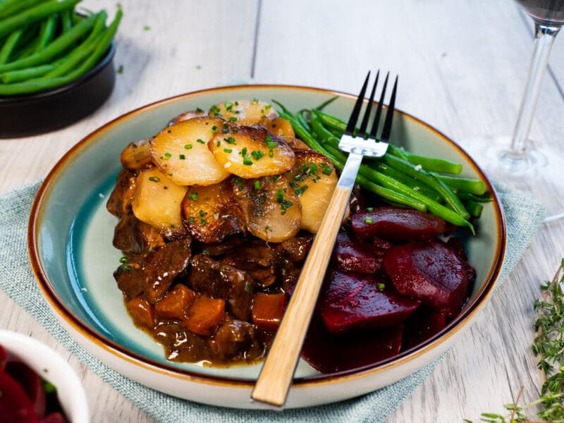 Plated lamb hotpot served with sliced potatoes and green beans