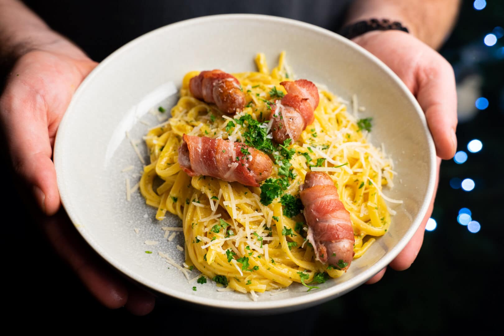 Bowl of garlic butter linguine topped with 4 pigs in blankets