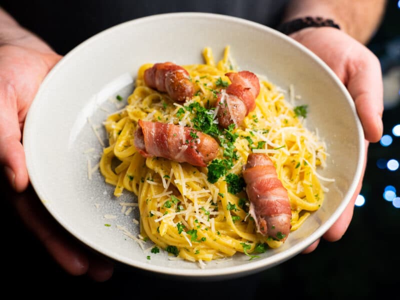 Bowl of garlic butter linguine topped with pigs in blankets